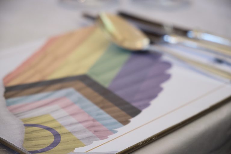 Placemat with table setting. The placemat is branded with the Inn's LGBTQ+ logo of a wing coloured by the progress flag