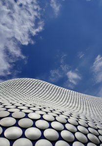 Close up of the texture of the Bullring Building in Birmingham beneath a blue sky with scattered clouds.