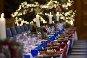 Festively decorated Christmas dinner table with candles, crackers, and glassware, set in front of a softly lit Christmas tree.