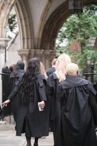Students in gowns photographed from behind, proceeding in line through Church Court