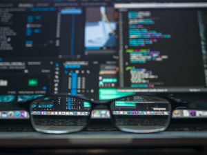 A picture of computer monitors showing code, with glasses in the foreground