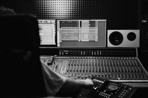 black and white shot of a mixing console and screen showing audio editing software