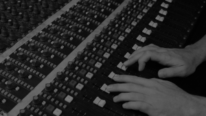 black and white angled shot from above of hands adjusting knobs on an audio mixing desk